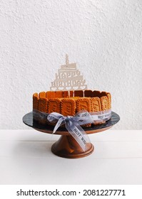 Kuala Lumpur, 15 Nov 2021 - A Lotus Biscoff Cheesecake On Black Cake Board And Wooden Cake Stand With White Background. The Cake Is Decorated With Light Grey Ribbon And A ' Happy Birthday' Cake Topper