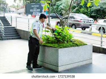 Kuala Lumpur, Malaysia, December 20, 2018: Residential Apartment Building Security Guard Pours Water Onto A Small Garden Bed