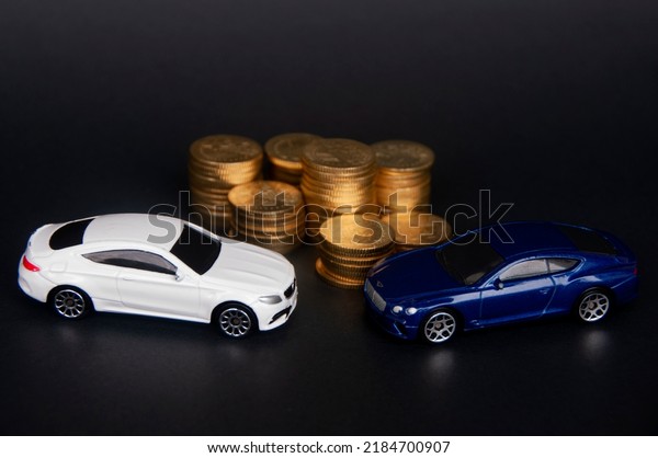 Kuala Lumpur, Malaysia - July\
2022 : Miniature toy car of Mercedes AMG and Bentley Continental GT\
with gold coins on black cover background. Wealth\
concept