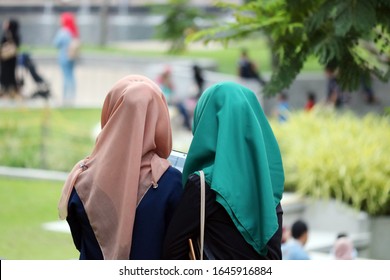 Kuala Lumpur, MY - APRIL 1, 2017: Back Viewing Of Two Female Young Kids In Colored Hijab, Sitting Inside The Local Public Garden.