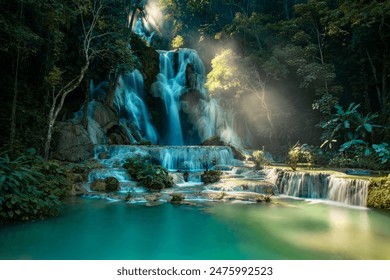 Kuang Si Waterfall in Laos. A beautiful waterfall surrounded by lush green trees and foliage, with a serene blue river flowing through it. - Powered by Shutterstock