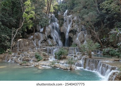 Kuang Si waterfall in Luang Prabang, Laos, flows into a Turquoise water with a lush green forest in the background.  - Powered by Shutterstock