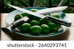 A kukri knife and a food knife crossing each other over a plate full of Gondhoraj Lemon on a wooden tray.