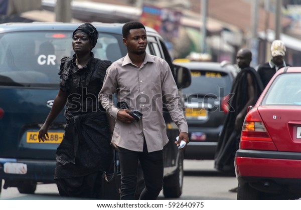 KUMASI, GHANA - Jan 16, 2017: Unidentified\
Ghanaian people walk along the road near driving cars. People of\
Ghana suffer  poverty due to the bad\
economy