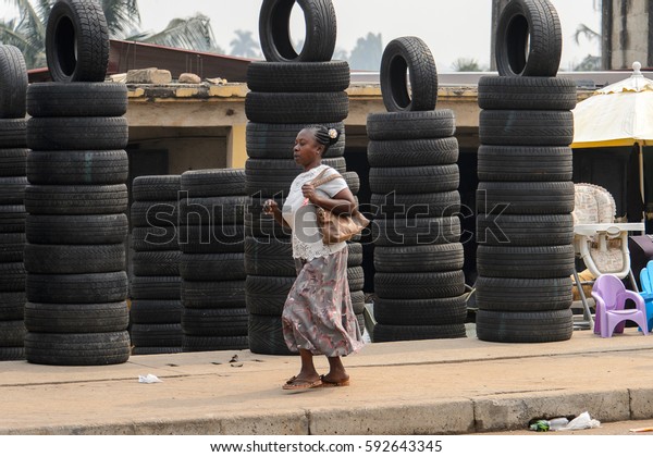 KUMASI, GHANA - Jan 16, 2017: Unidentified\
Ghanaian old woman walks by the heap of car tires. People of Ghana\
suffer  poverty due to the bad\
economy