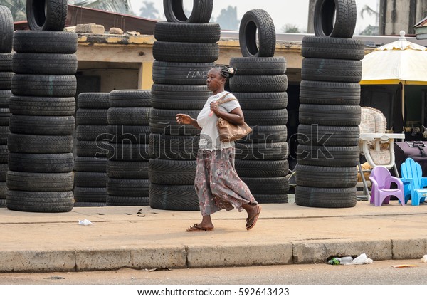 KUMASI, GHANA - Jan 16, 2017: Unidentified\
Ghanaian old woman walks by the heap of car tires. People of Ghana\
suffer  poverty due to the bad\
economy