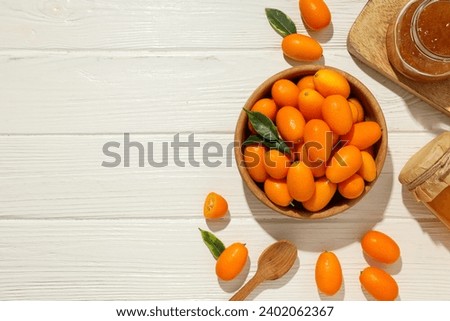 Kumquat in bowl and jars of jam on light wooden background, space for text