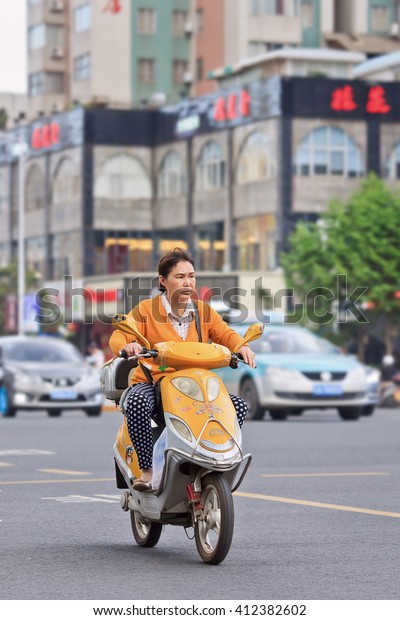 KUNMING, CHINA-JUNE 30, 2014. Woman on yellow\
electric bike. Many electric bikes in China are the scooter style\
e-bike that may or may not have pedals. The Chinese e-bike market\
is the largest in the\
world.
