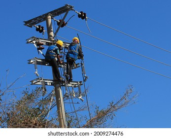 Kupang, Indonesia - April 9, 2021: Two Electricians Repair A Broken Power Line On A Sloping Utility Pole After A Tropical Cyclone