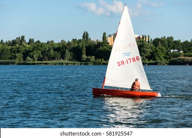 KURCHATOW, RUSSIA - JUNE 23, 2016: Man on sailing boat and windsurfer train on the lake.