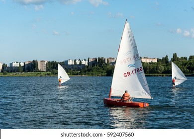 KURCHATOW, RUSSIA - JUNE 23, 2016: Man on sailing boat and windsurfer train on the lake.