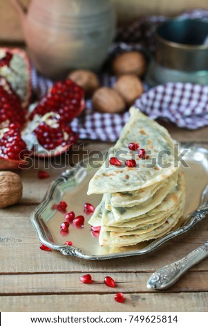 Kutabs - herbs or meat stuffed flatbreads served with pomegranate seeds on a wooden rustic background. Azerbaijan traditional cuisine. Vegan food. 