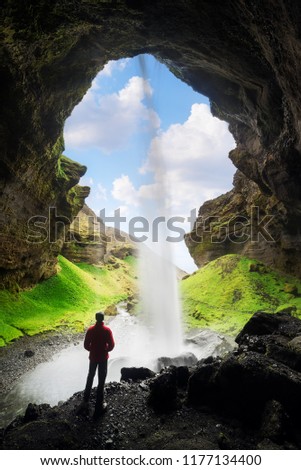 Kvernufoss waterfall in the gorge of the mountains. Tourist Attraction Iceland. Man in red jacket standing and looks at the flow of falling water. Beauty in nature