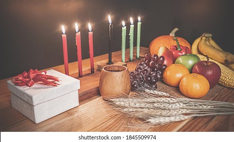 Kwanzaa holiday concept with decorate seven candles red, black and green, gift box, pumpkin,corn and fruit on wooden desk and black background. - Powered by Shutterstock