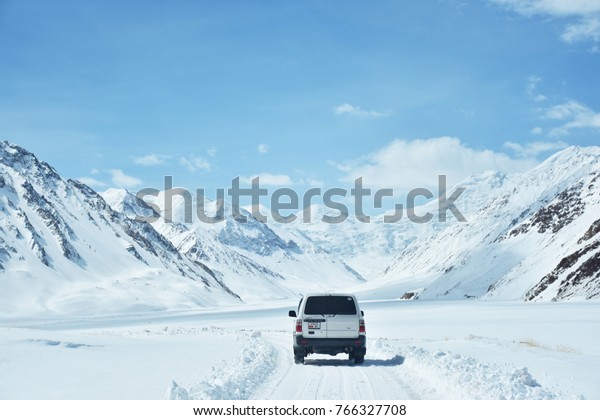  Kygyzstan-Tajikistan Border- April 15, 2017: Snow\
capped road among mountains with white Toyota Land Cruiser off road\
driving on The Pamir Highway, border from Kygyzstan to\
Tajikistan,central asia  