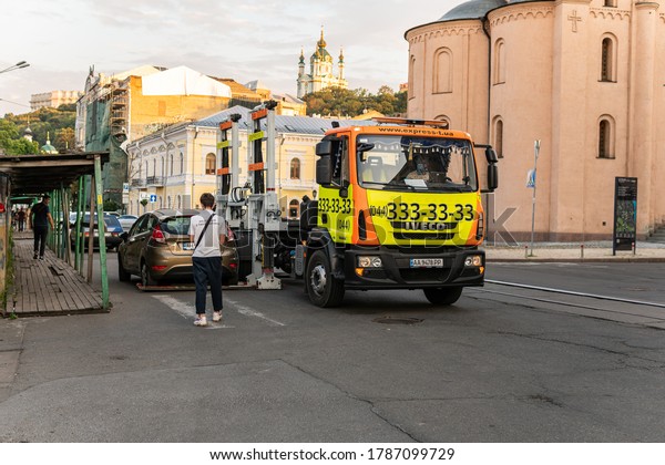 Kyiv (Kiev),\
Ukraine - July 30, 2020: A breakdown truck, tow car, wrecker,\
recovery vehicle is evacuating a car for a parking violation and an\
inspector is issuing a\
fine