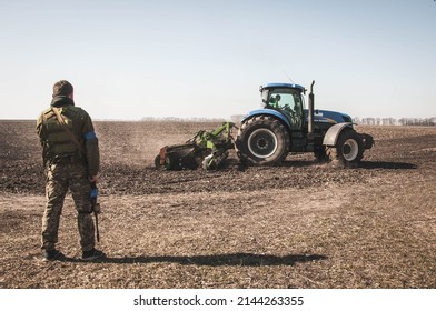 Kyiv, Ukraine - 03 23 2022: Ukrainian soldier of territorial defense looks at the tractor plowing the field during the Russian-Ukrainian war