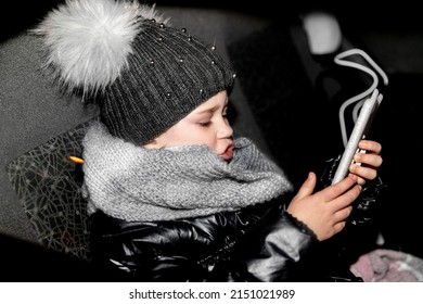 Kyiv Ukraine 12 15 2020 Little Girl Looking At The Phone In The Car, Clothes Warm, Window Open, Night, Light Skin, Blue Eyes