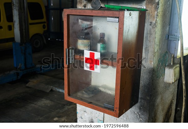 Kyiv, Ukraine - 12 May 2021: Old first aid kit\
cabinet with some medications and red cross sign. Old car garage\
interior.