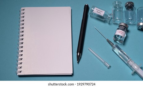 Kyiv, Ukraine - 2020. Blank Notebook With Pen On A Blue Background. Empty Vaccine Vials And A Syringe With A Needle Lie On The Table. Concept: Vaccine, Injection, Money, Counting.