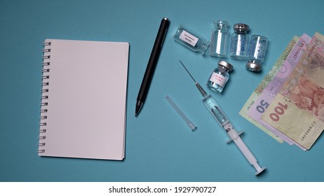 Kyiv, Ukraine - 2020. Blank Notebook With Pen On A Blue Background. Empty Vaccine Vials And A Syringe With A Needle Lie On The Table. Concept: Vaccine, Injection, Money, Counting.