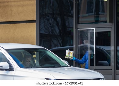 Kyiv Ukraine - April 01 2020: A Worker In A Protective Mask And Protective Gloves Issues An Order Through A Secure Window In A Fast Food Restaurant. Quarantine Time, Coronavirus Protection Measures.