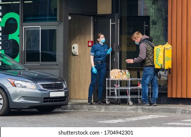 Kyiv Ukraine - April 10 2020: Workers In Protective Masks And Protective Gloves Pass Orders To A Delivery Service Representative In A Fast Food Restaurant. Quarantine In Large Cities.