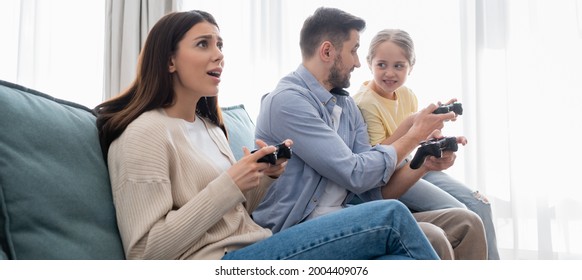 KYIV, UKRAINE - APRIL 8, 2021: Tense Woman Gaming With Joystick Near Family, Banner