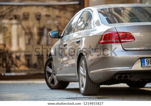 KYIV, UKRAINE - August 25, 2018: Rear view\
detail of silver shiny car parked on pedestrian zone pavement on\
background of blurred city buildings. Modern city lifestyle,\
parking problems concept.