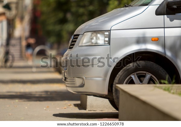 KYIV, UKRAINE - August 25, 2018: Front view\
detail of silver shiny car parked on pedestrian zone pavement on\
background of blurred urban landscape. Modern city lifestyle,\
parking problems concept.