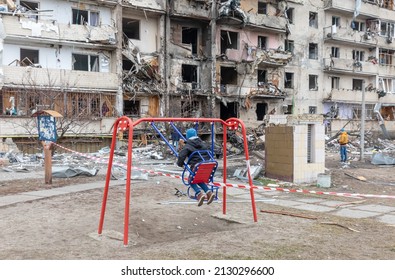 KYIV, UKRAINE - Feb. 25, 2022: War of Russia against Ukraine. Child on a swing against a residential building damaged by russian rocket in a residential area of Kyiv. Russian world in Ukraine