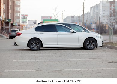 Kyiv, UKRAINE- February 27, 2019: Side view of white car parked in paved parking lot area on blurred suburb road background on bright sunny day. Transportation and parking concept.