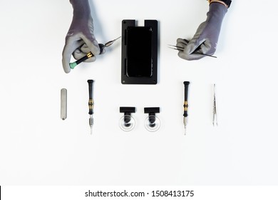 KYIV, UKRAINE - FEBRUARY 27 2019: Process of Smartphone Display Repair Flat Lay Maintenance Tool with Copy Space on White Background. Engineer Hands in Gloves Fix Cellphone Broken Glass