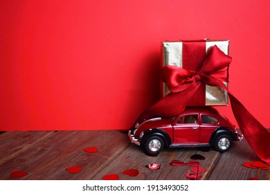 Kyiv, Ukraine - Febuary 10, 2021: Gift On The Roof Of A Red Car On A Red Background. February 14 Card, Valentine's Day. Flower Delivery. 8 March, International Happy Women's , Christmas