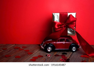 Kyiv, Ukraine - Febuary 10, 2021: Gift On The Roof Of A Red Car On A Red Background. February 14 Card, Valentine's Day. Flower Delivery. 8 March, International Happy Women's , Christmas