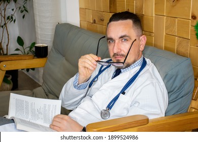 KYIV, UKRAINE, - JANUARY 15, 2021: Doctor Caucasian With Book In His Hands And Phonendoscope Around His Neck Is Resting,  Studying New Disease Or Method Of Medical Diagnostics In Hospital Break Room