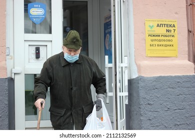 Kyiv, Ukraine - January 24 2022: Elderly Man Wearing Face Mask Carrying Plastic Bag And Cane Walking Out Of A Pharmacy Store