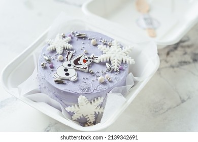 KYIV, UKRAINE - JANUARY 24: Frozen Character On Cake With Blue Cream Cheese Frosting Decorated With Snowflakes And Olaf Snowman. Winter Cake On White Background. Korean Trendy Bento Cake