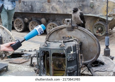 KYIV, UKRAINE - June 23, 2022: Exposition Of Russian Military Equipment Destroyed In Russian Invasion Of Ukraine. City Crow On Hatch Of Wrecked Combat Vehicle And Hand With Microphone In Front Of Her
