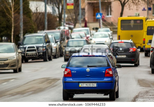 KYIV, UKRAINE - March 30, 2018: New blue car moving\
fast along the clean city road on bright sunny day past zebra by\
parking cars and buildings of town. Speed, comfort, traveling in\
modern life.