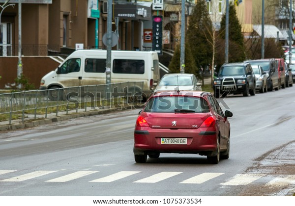 KYIV, UKRAINE - March 30, 2018: New red car moving\
fast along the clean city road on bright sunny day past zebra by\
parking cars and buildings of town. Speed, comfort, traveling in\
modern life.