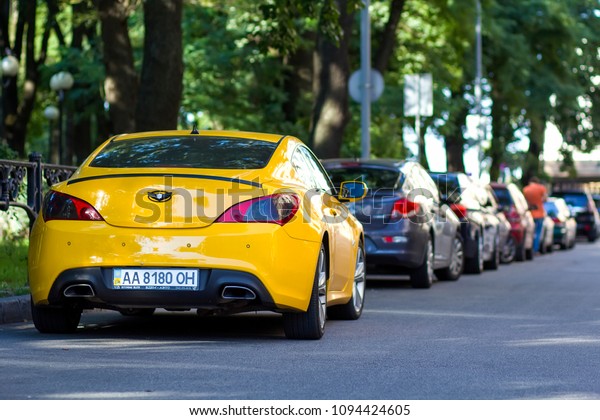 KYIV, UKRAINE - March 30, 2018: Long row of cars\
parking along a city road under shadow of big trees on bright\
summer day. Transportation, parking problems and technology\
concept.