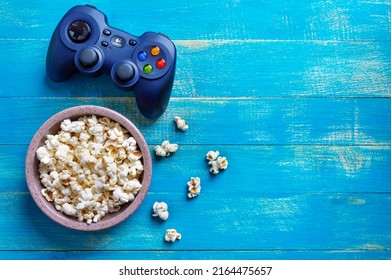 KYIV, UKRAINE - MAY 23, 2022: Gamepad LOGITECH, bowl of popcorn on blue wooden background with copy space. Top view. The concept of leisure, games, pastime