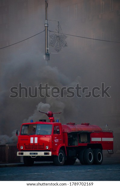 Kyiv, Ukraine - MAY 5 2020: Red fire truck KAMAZ\
takes part in the extinguishing of a big fire on the street of\
Kyiv. Fire car at work against the background of the black smoke.\
Space for text.