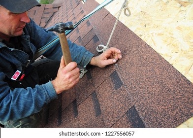 KYIV, UKRAINE - November, 12, 2018: Roofing contractor laying asphalt shingles.  Roofer with protection rope, safety kit on the house roof installing, repair asphalt shingles. 