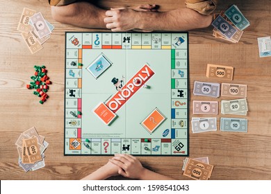 KYIV, UKRAINE - NOVEMBER 15, 2019: Top View Of Man And Woman Playing Monopoly At Wooden Table