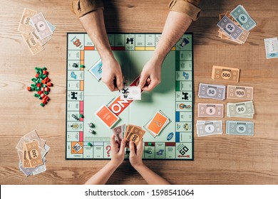 KYIV, UKRAINE - NOVEMBER 15, 2019: Cropped View Of Man Holding Explanation Card And Woman With Toy Currency While Playing In Monopoly Game