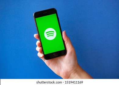 Kyiv, Ukraine - October 1, 2019: Studio shot of hand holding Apple iPhone 8 with Spotify logotype on a screen. Isolated on a blue paper background.