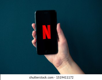 Kyiv, Ukraine - October 1, 2019: Studio shot of hand holding Apple iPhone 8 with Netflix logotype on a screen. Isolated on a black paper background.