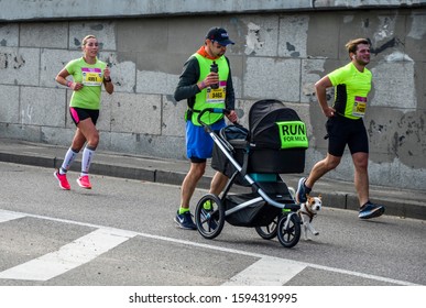 KYIV, UKRAINE - OCTOBER 6, 2019: Male Runner Dad Running City Marathon With Baby Carriage And Dog. Run For Fun